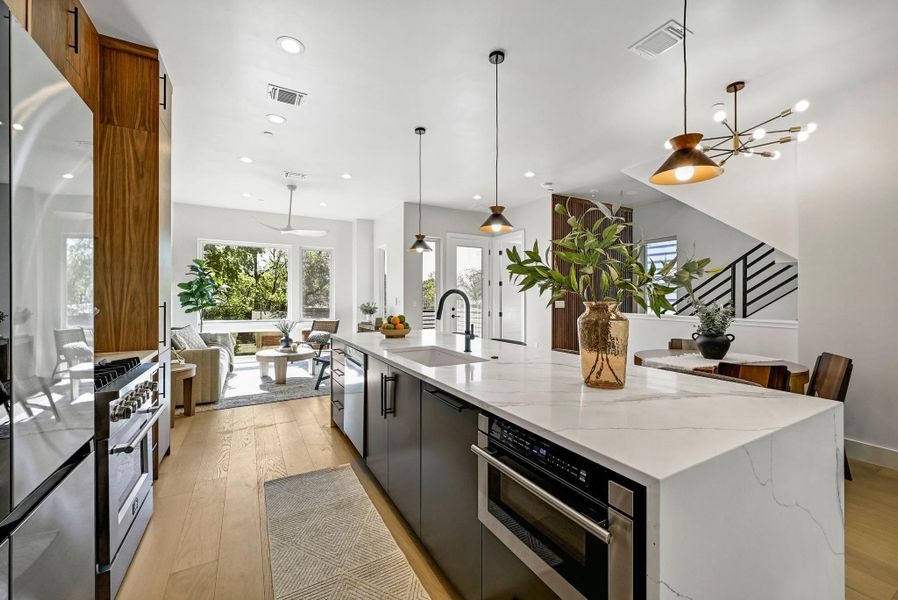 Kitchen featuring custom wood cabinets, quartz waterfall countertop with breakfast bar area, and high end stainless steel appliances. (This is Unit #2 - each Unit has the same layout, however a few differing details such as light fixtures, custom cabinet/backsplash/tile colors)