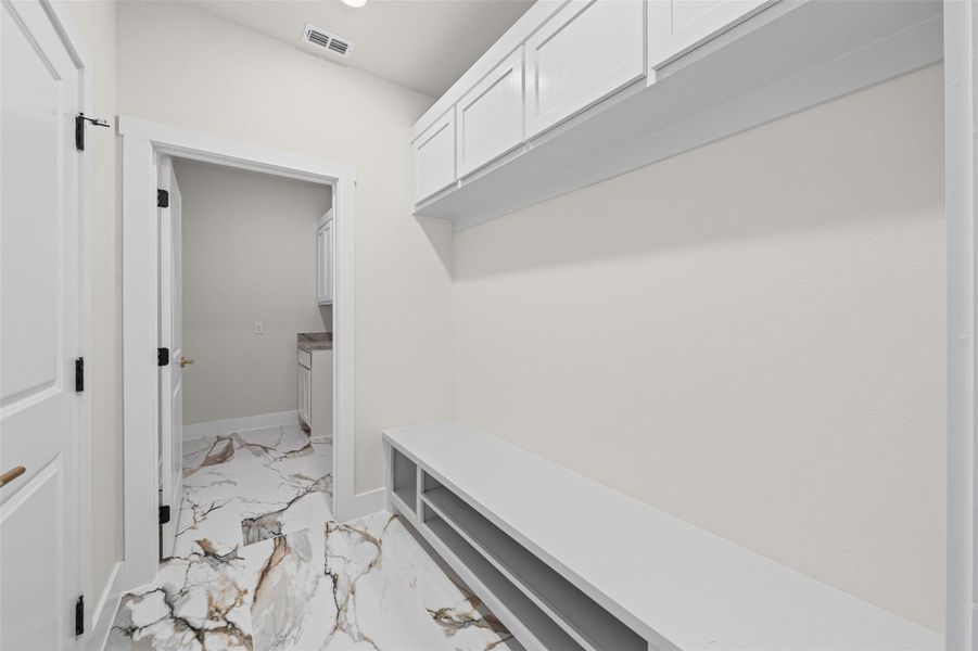 An organized entryway mudroom features custom built-in cabinetry and polished marble-look tile flooring.