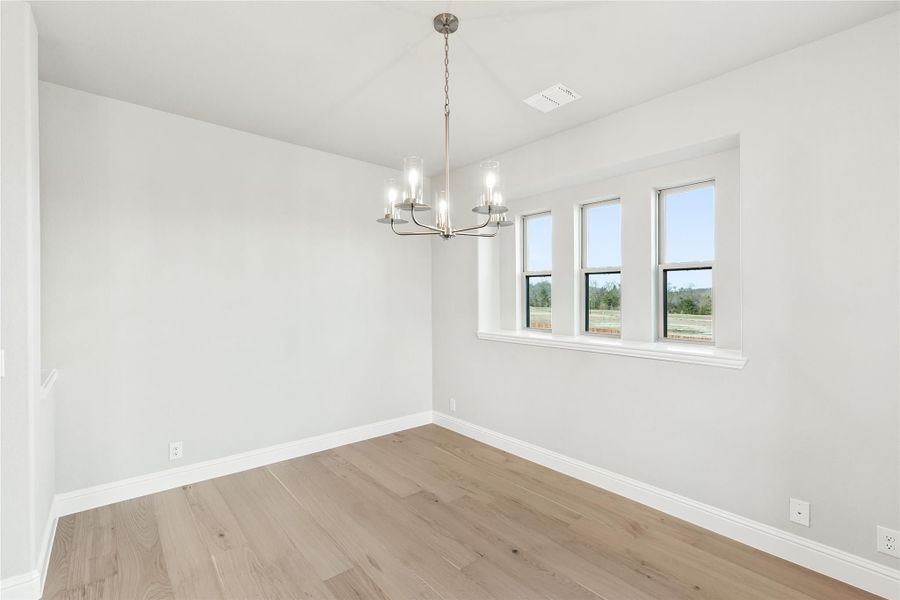 Empty dining room with light hardwood floors, chandelier, and three windows with outdoor views Empty dining room with light hardwood floors, chandelier, and three windows with outdoor views