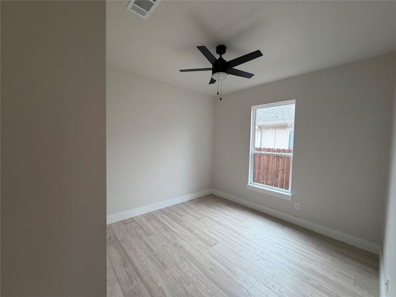 A well-lit bedroom features durable plank flooring and a modern ceiling fan for comfort.