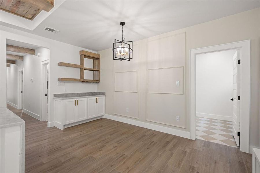 Open-concept living area featuring wood-finish flooring, a built-in dry bar with wood shelving and lower cabinetry, and a geometric chandelier