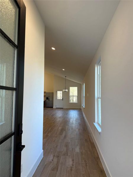Hallway with wood finished floors, vaulted ceiling, and recessed lighting