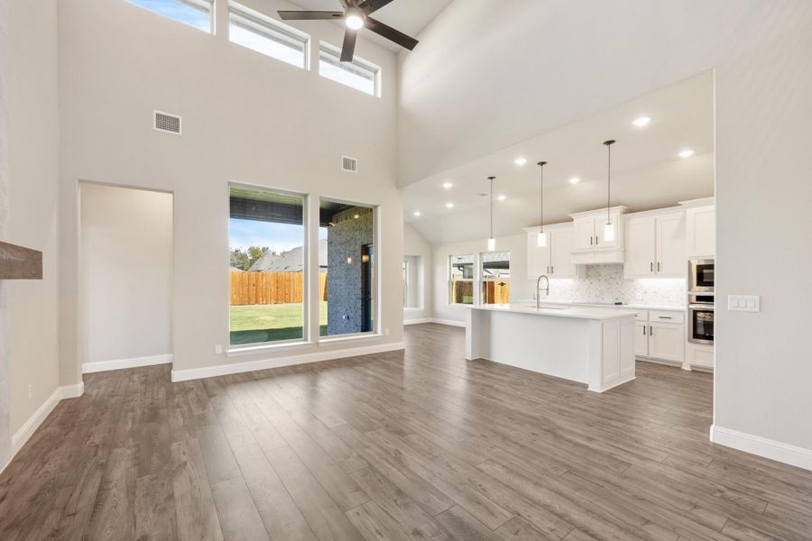 Open-concept living area with high ceilings, hardwood floors, and white kitchen with island and pendant lights Open-concept living area with high ceilings, hardwood floors, and white kitchen with island and pendant lights