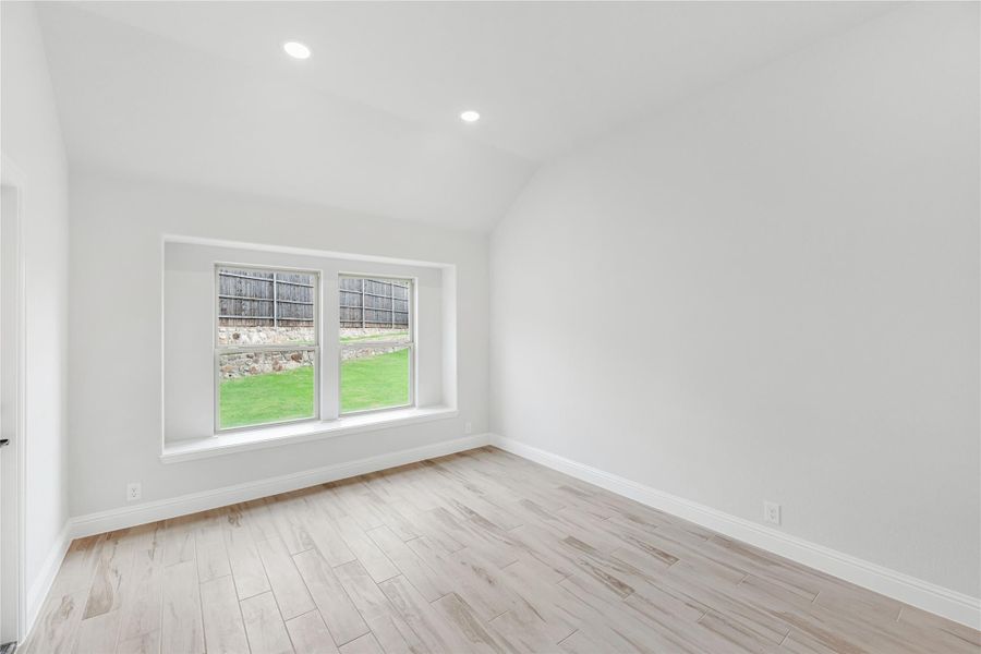 Empty room with vaulted ceiling, light wood floors, and double windows overlooking a backyard Empty room with vaulted ceiling, light wood floors, and double windows overlooking a backyard