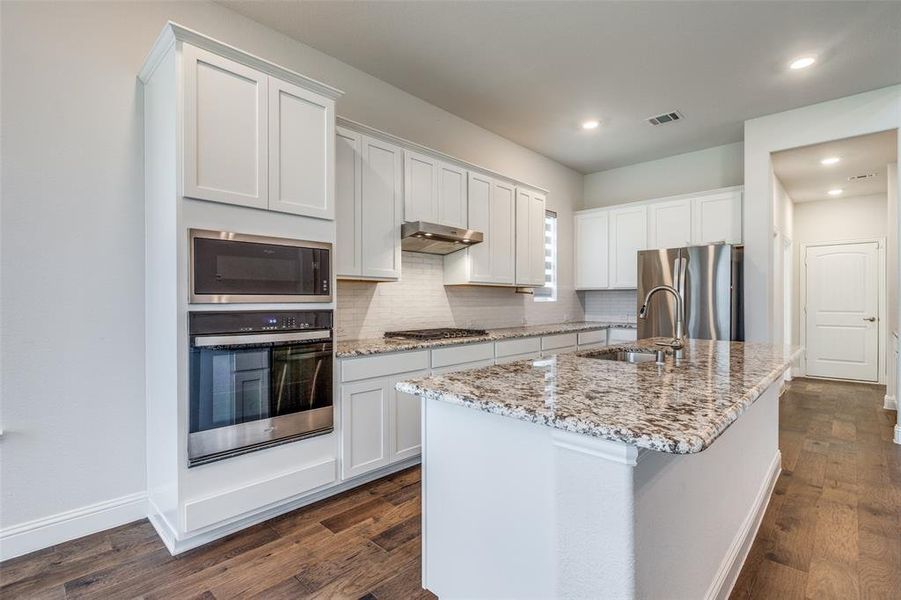 Kitchen with stainless steel appliances, a sink, under cabinet range hood, decorative backsplash, and dark wood-type flooring