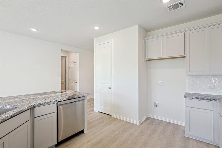 Kitchen featuring sink, light stone countertops, light wood-type flooring, appliances with stainless steel finishes, and tasteful backsplash