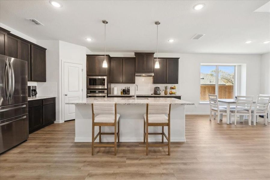 Kitchen featuring sink, hanging light fixtures, light hardwood / wood-style flooring, a center island with sink, and appliances with stainless steel finishes