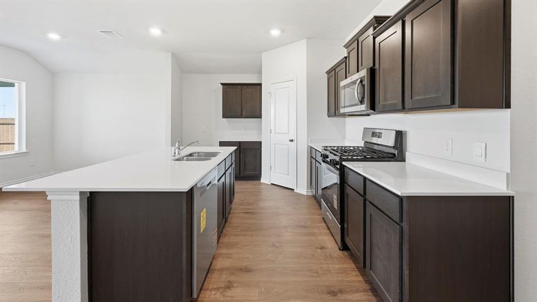 Kitchen featuring stainless steel appliances, an island with sink, light wood finished floors, dark brown cabinetry, and recessed lighting
