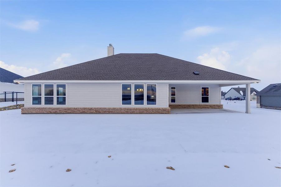 Snow covered back of property with a chimney, a patio, brick siding, and roof with shingles Snow covered back of property with a chimney, a patio, brick siding, and roof with shingles