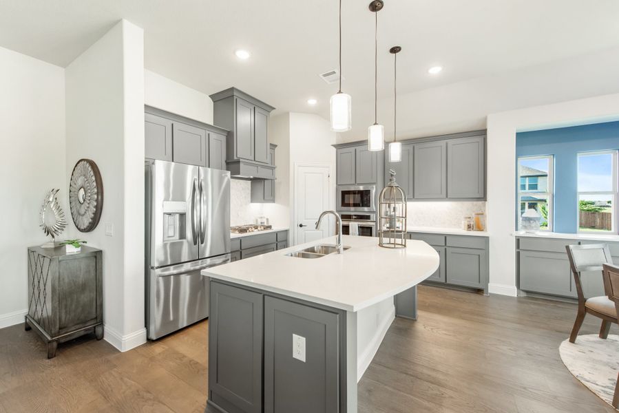 Kitchen with gray cabinets, center island with sink, stainless steel appliances, and hardwood floors