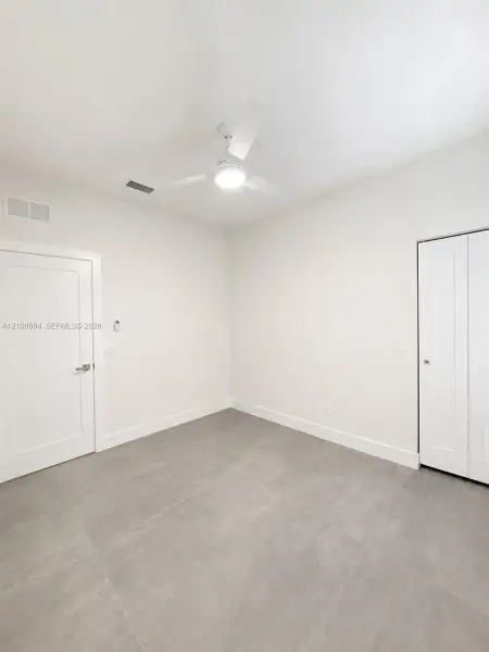 Neutral-toned interior featuring large-format tile flooring, a minimalist white ceiling fan with an integrated light fixture, and classic panel doors