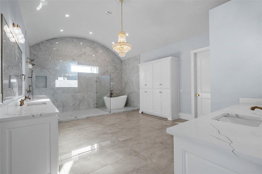 Full bathroom with double vanity, a freestanding bath, vaulted ceiling, a marble finish shower, and light marble finish floors Full bathroom with double vanity, a freestanding bath, vaulted ceiling, a marble finish shower, and light marble finish floors