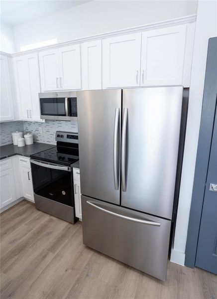 Kitchen with light wood-type flooring, white cabinetry, stainless steel appliances, and tasteful backsplash