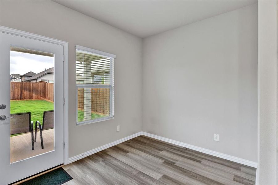 This space features durable plank flooring, a window with blinds providing natural light, and a door leading to a patio and a fenced yard with a lawn