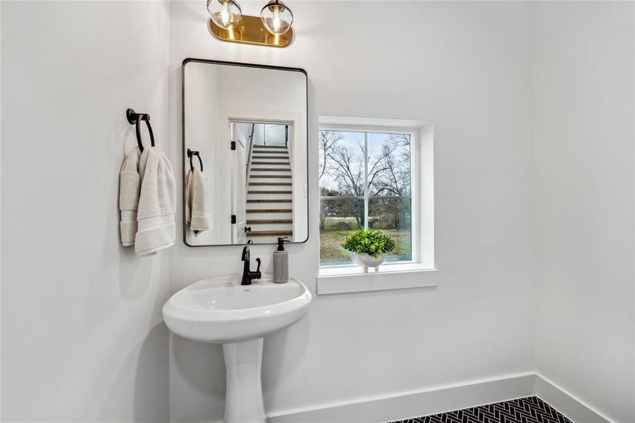 Chic powder room featuring a modern pedestal sink, stylish lighting, and a bright window view. Perfect for guests!