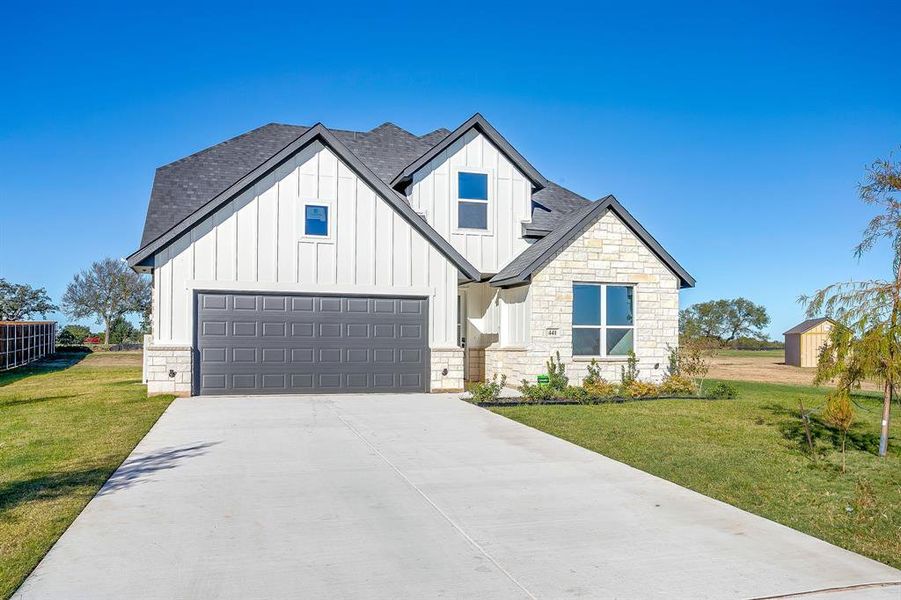 View of front of home with board and batten siding, roof with shingles, driveway, and stone siding