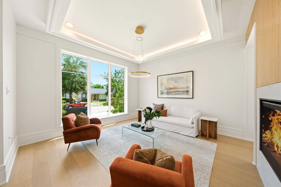 Elegant front living room featuring tray ceilings, oversized windows, and a sleek double-sided fireplace. Elegant front living room featuring tray ceilings, oversized windows, and a sleek double-sided fireplace.