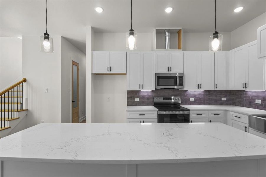 The kitchen features a large island with a light-colored countertop, white cabinetry with dark handles, and a stainless steel range and microwave