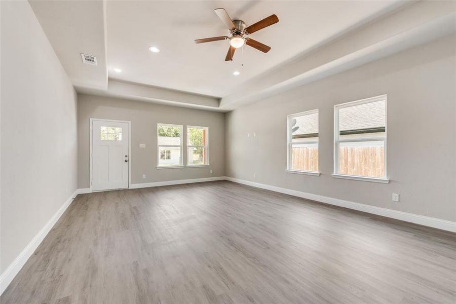 Unfurnished living room with a tray ceiling, light hardwood / wood-style floors, and ceiling fan