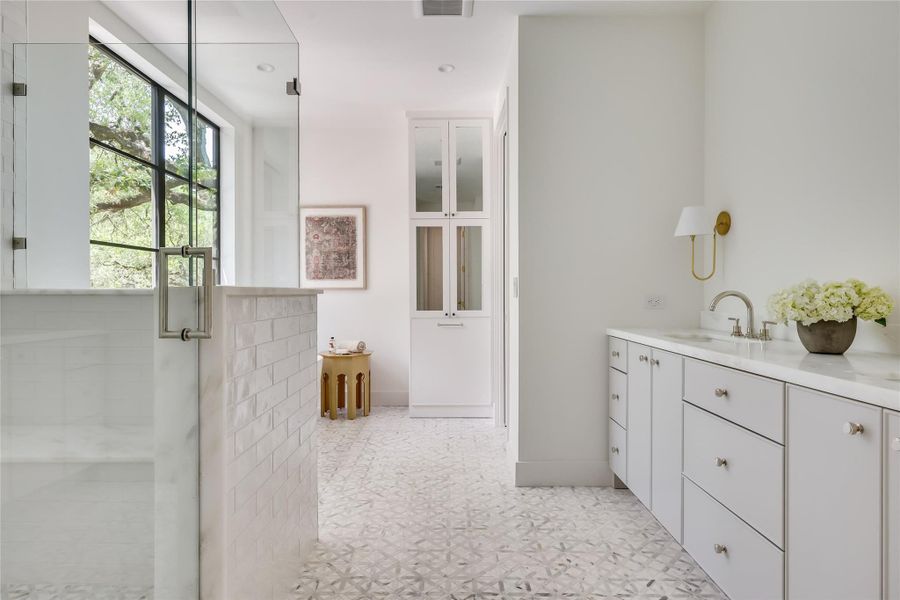 Spacious bathroom featuring a glass-enclosed shower with a black-framed window, white subway tile wall, patterned floor tile, and an extensive vanity with dual sinks