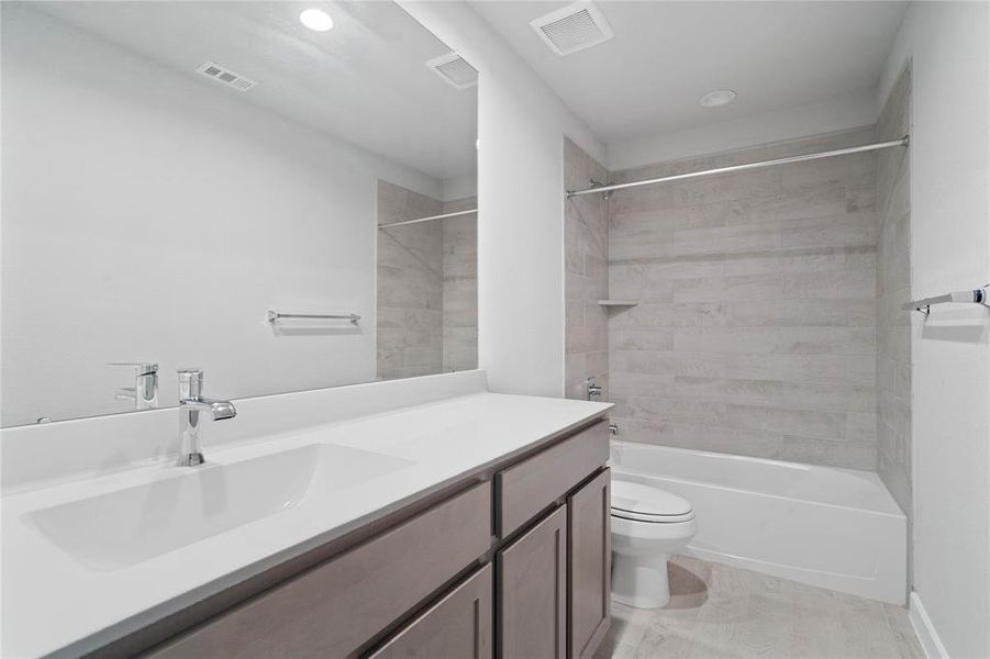 Secondary bath features tile flooring, bath/shower combo with tile surround, wood cabinets, beautiful light countertops, mirror, dark, sleek fixtures and modern finishes!