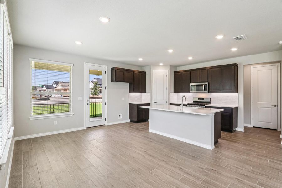 Kitchen with light countertops, dark brown cabinetry, appliances with stainless steel finishes, light wood-style flooring, and an island with sink