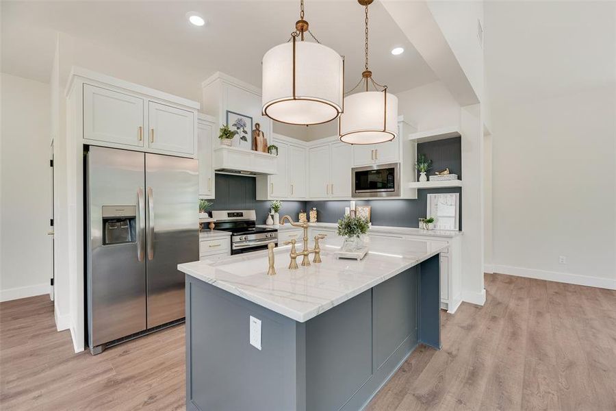 Kitchen with appliances with stainless steel finishes, white cabinets, gray cabinets, an island with sink, and light wood-style floors
