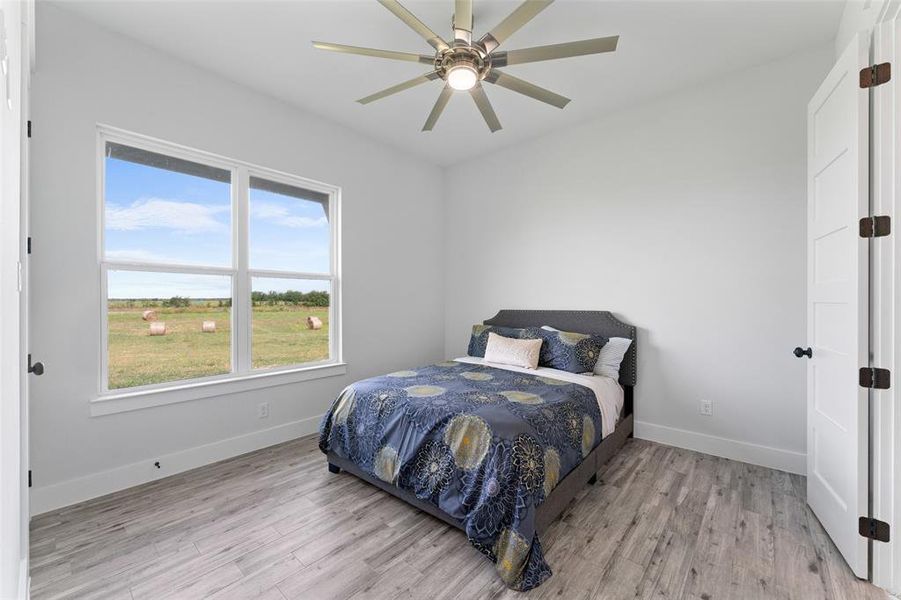 Bright interior space featuring a large window with white trim, wood-finish flooring, a contemporary ceiling fan with integrated lighting, and a white paneled door with dark hardware
