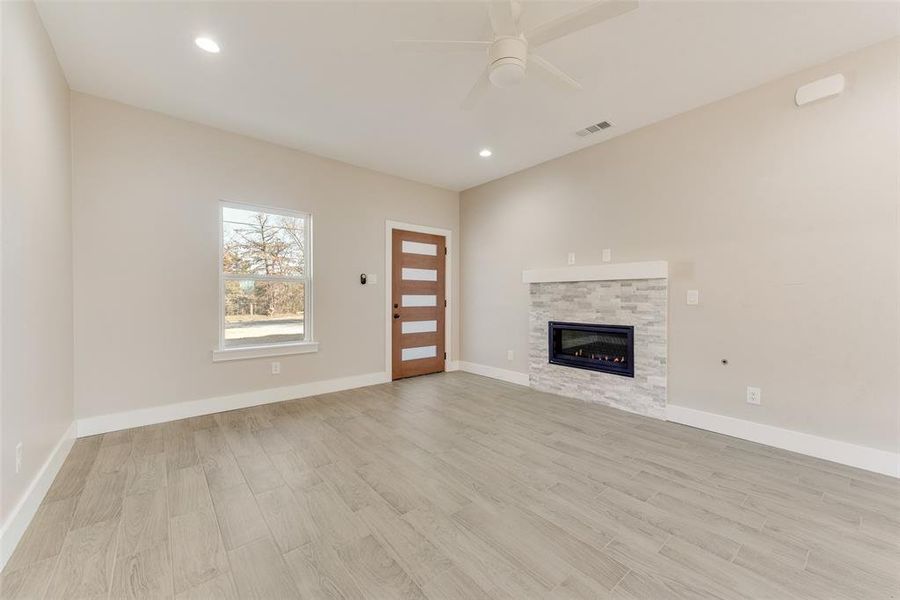 Unfurnished living room featuring a stone fireplace, ceiling fan, and light hardwood / wood-style flooring