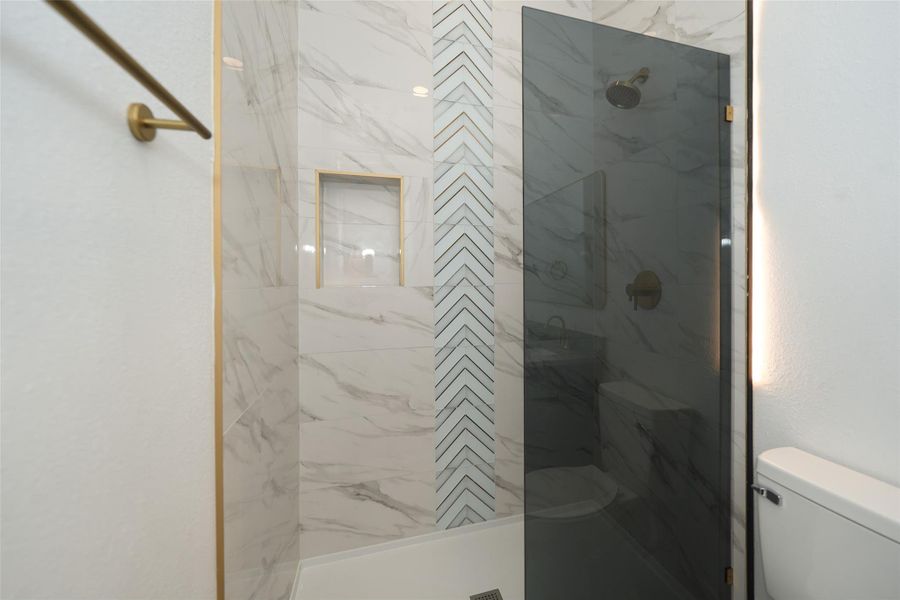 This modern bathroom features a spacious walk-in shower with elegant marble-style tiling. It includes a double vanity with sleek black fixtures and a granite countertop, providing a stylish and functional space. The room is bright with a clean, contemporary design.