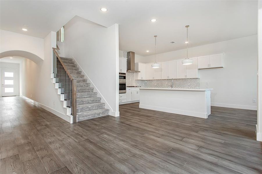 Kitchen with wall chimney range hood, backsplash, pendant lighting, a kitchen island with sink, and white cabinets