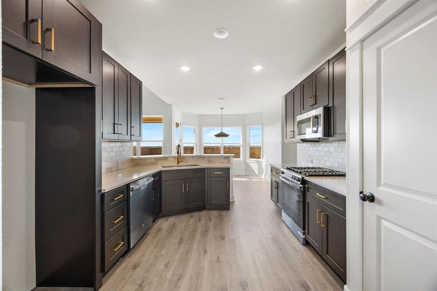 Kitchen featuring appliances with stainless steel finishes, hanging light fixtures, a peninsula, light wood-style floors, and light stone countertops