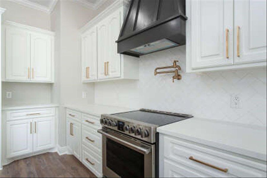 Kitchen with stainless steel range, premium range hood, white cabinets, ornamental molding, and dark wood-style floors