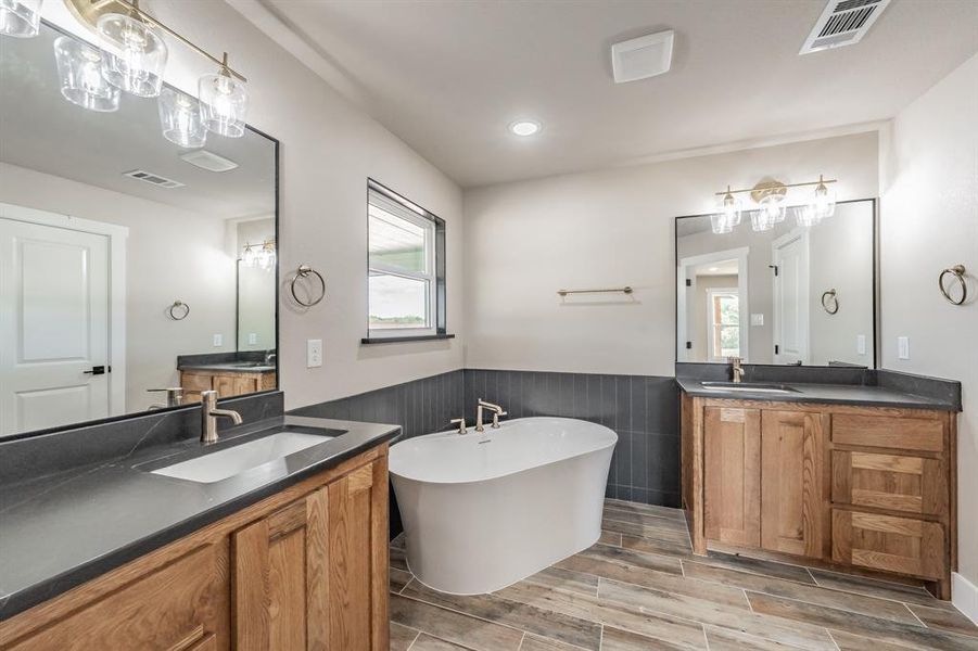 Full bathroom with two vanities, a soaking tub, wood finish floors, wainscoting, and recessed lighting Full bathroom with two vanities, a soaking tub, wood finish floors, wainscoting, and recessed lighting