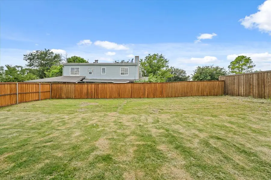 Expansive backyard featuring a manicured lawn, full wood fencing, and mature perimeter trees