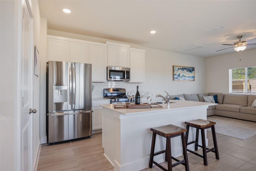 Kitchen featuring stainless steel appliances, open floor plan, backsplash, white cabinets, and a kitchen breakfast bar Kitchen featuring stainless steel appliances, open floor plan, backsplash, white cabinets, and a kitchen breakfast bar