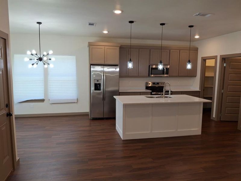 Kitchen featuring stainless steel appliances, a chandelier, decorative light fixtures, a kitchen island with sink, and dark wood finished floors Kitchen featuring stainless steel appliances, a chandelier, decorative light fixtures, a kitchen island with sink, and dark wood finished floors