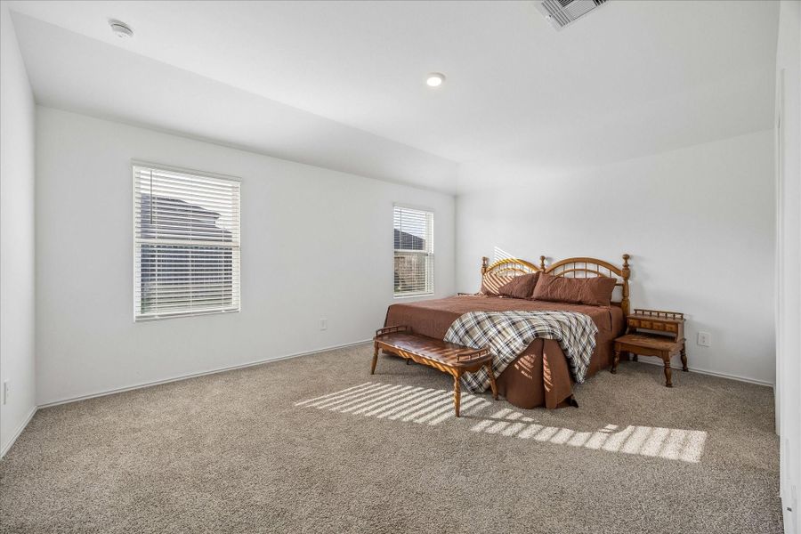 Spacious primary bedroom with neutral carpeting, two large windows allowing ample natural light.