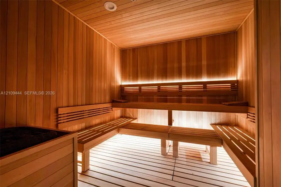 Sauna featuring wood-plank wall paneling, multi-level slatted wood benches, hidden LED accent lighting, and a built-in heating unit