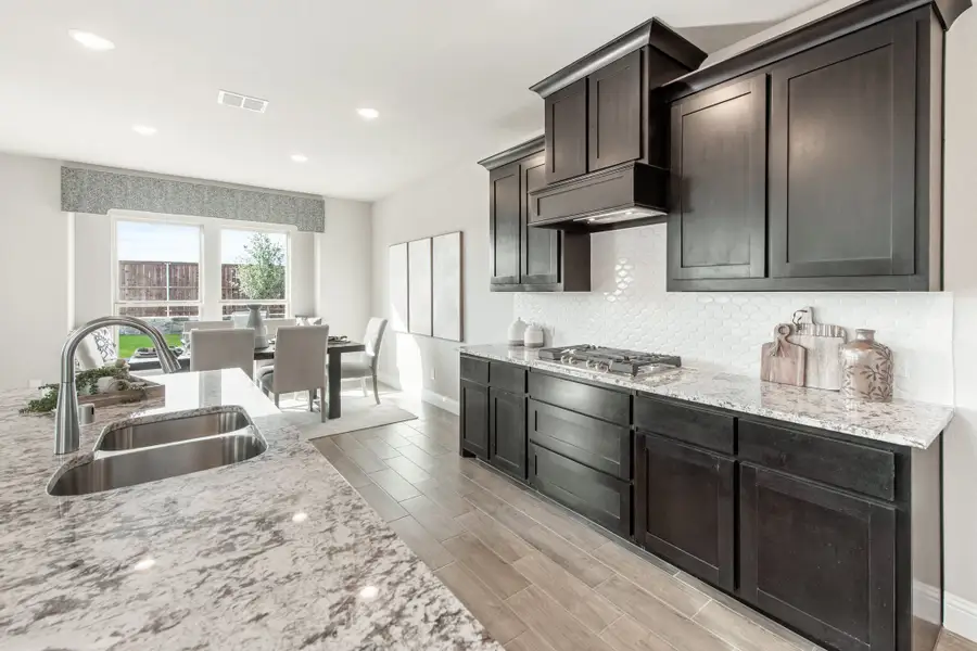 Kitchen with dark cabinets, granite countertops, stainless sink, and gas cooktop open to dining area Kitchen with dark cabinets, granite countertops, stainless sink, and gas cooktop open to dining area