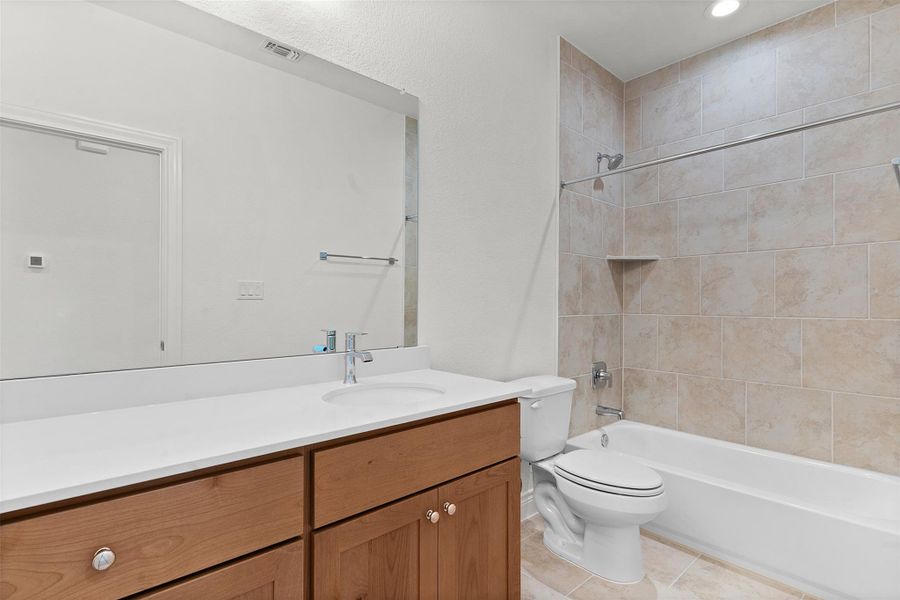 Bathroom featuring a single vanity with wood cabinetry and a white countertop, an integrated sink with a chrome faucet, a large frameless mirror, and a tiled shower-bathtub combination with a built-in shelf