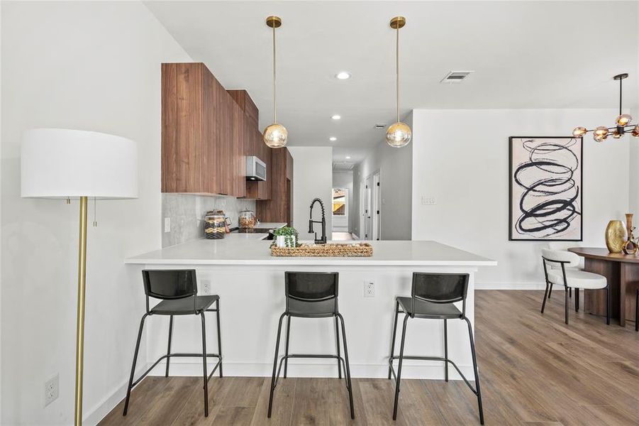 Kitchen with hardwood / wood-style floors, a breakfast bar, decorative backsplash, decorative light fixtures, and kitchen peninsula