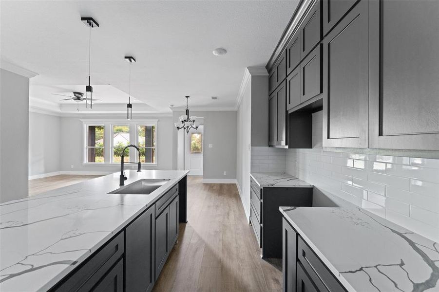 Kitchen featuring light stone counters, light wood-style floors, crown molding, decorative light fixtures, and backsplash