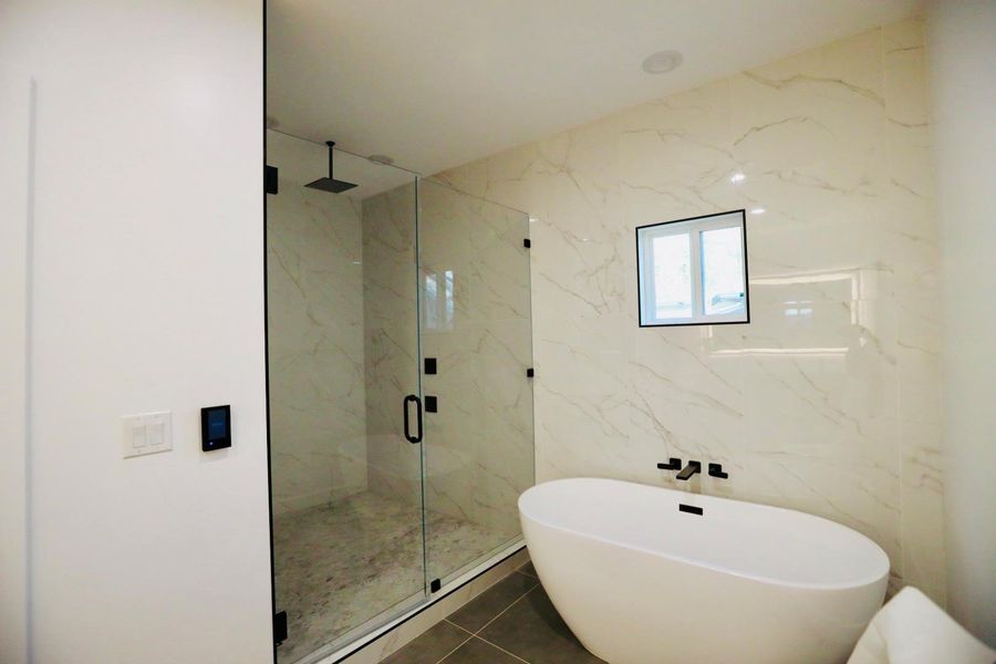 Bathroom with a marble finish shower, a soaking tub, and dark tile patterned floors
