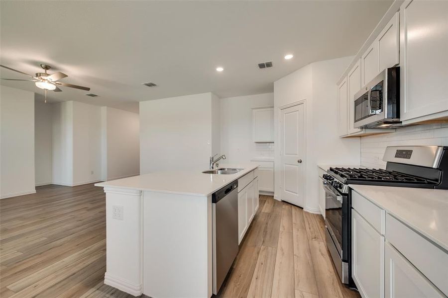 Kitchen featuring ceiling fan, light hardwood / wood-style flooring, stainless steel appliances, backsplash, and a kitchen island with sink