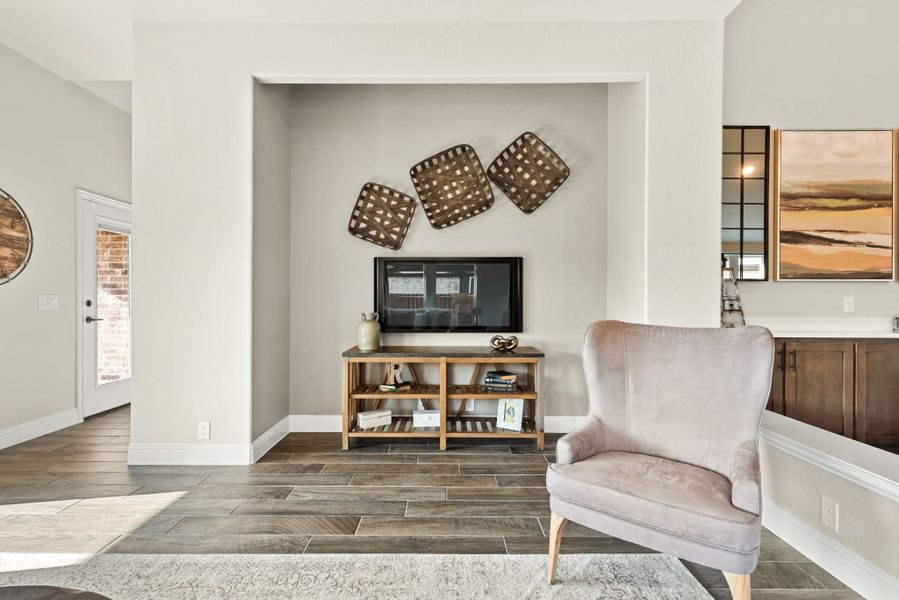 Living area with wall-mounted TV, wooden media console, and upholstered accent chair on wood-look tile floors