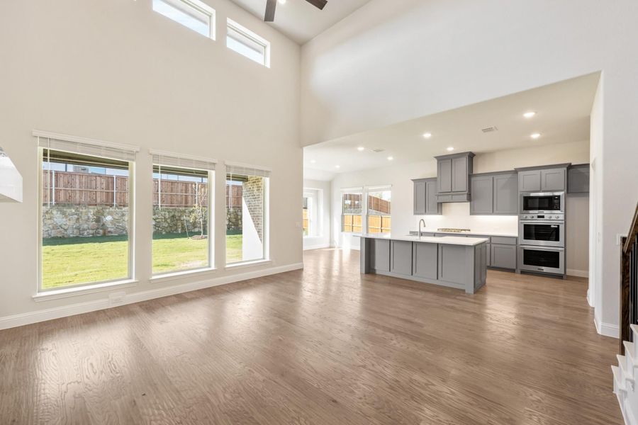 Open living area with high ceilings and hardwood floors leading to kitchen with gray cabinets and center island Open living area with high ceilings and hardwood floors leading to kitchen with gray cabinets and center island