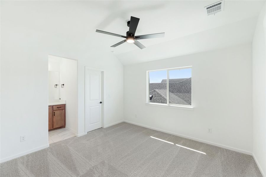 Bedroom with vaulted ceiling, black ceiling fan, carpet flooring, and ensuite bathroom access.