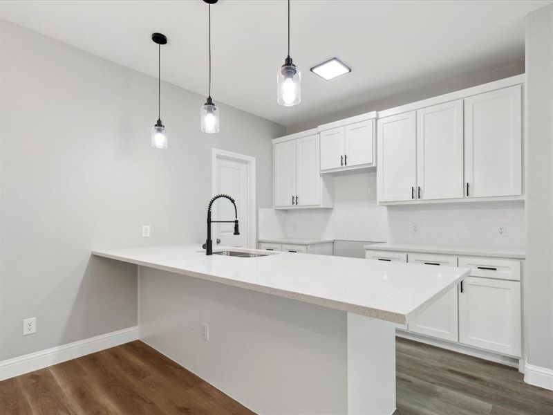 Kitchen with kitchen peninsula, white cabinetry, dark wood-type flooring, sink, and pendant lighting