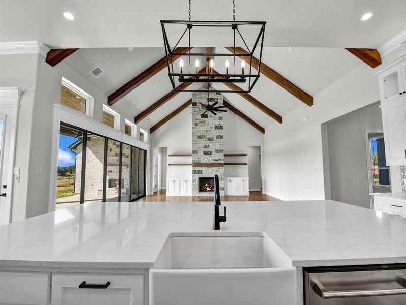 Kitchen with light stone countertops, sink, white cabinets, and a stone fireplace